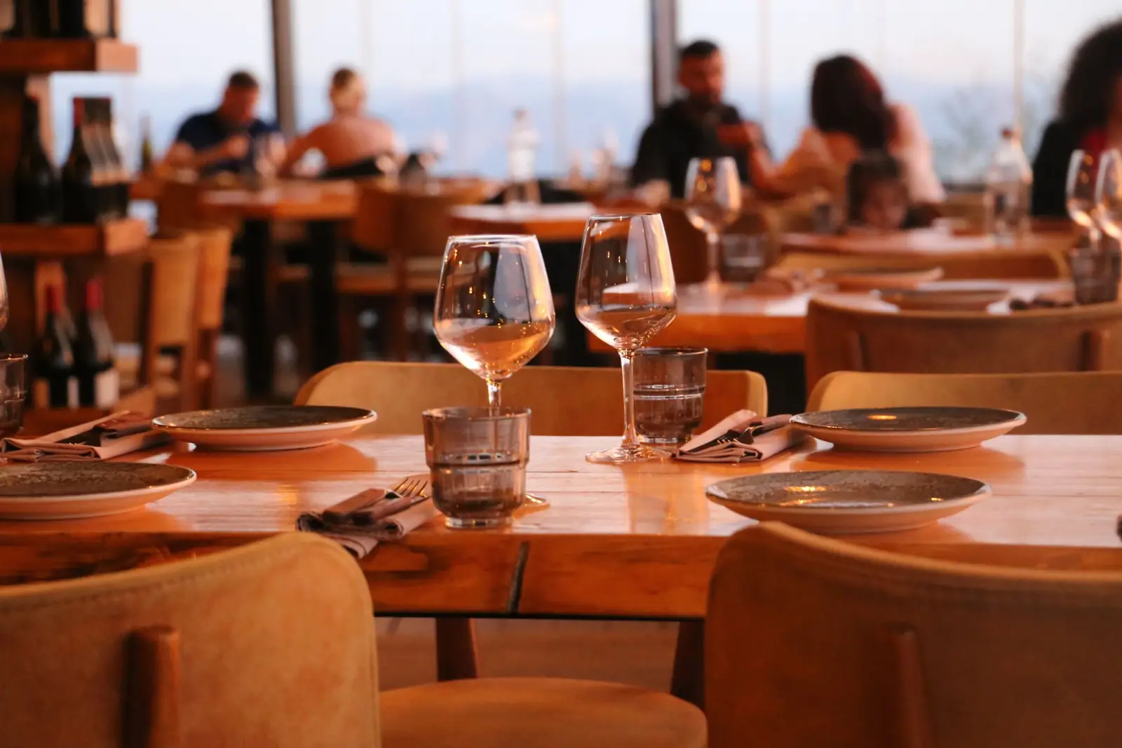 Set wooden tables in a warm restaurant, guests dining by the windows