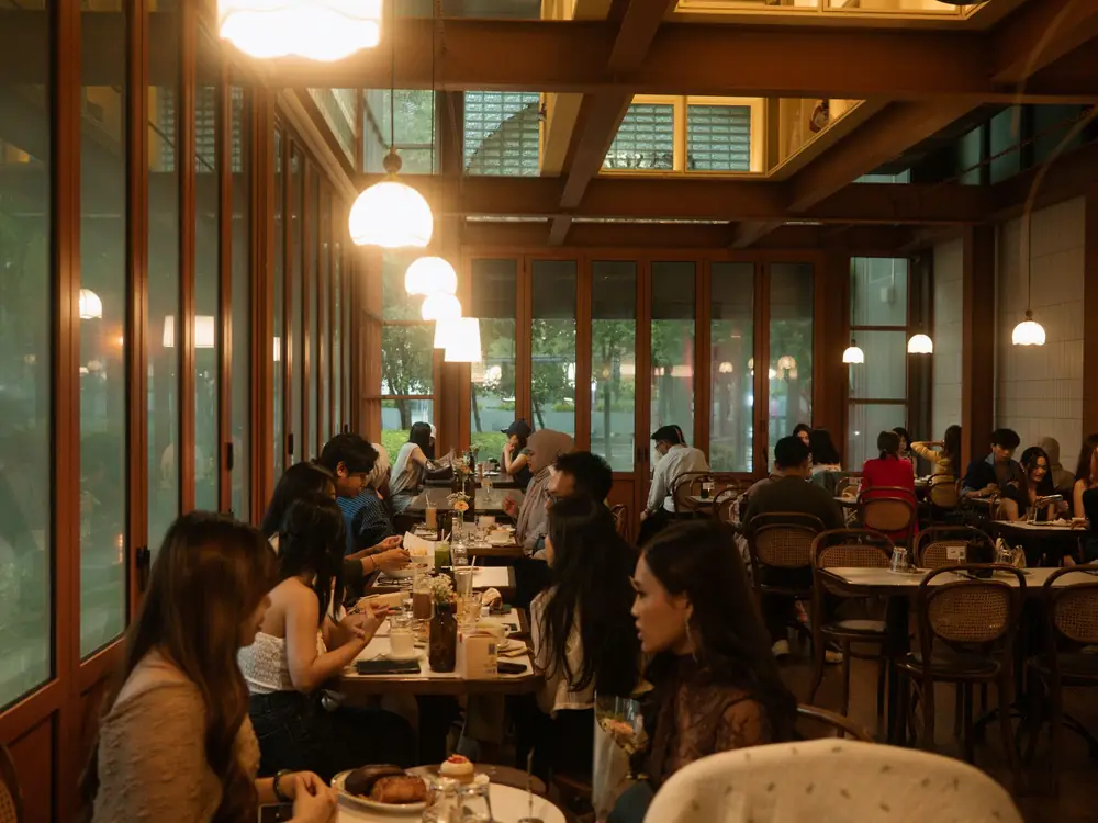 Diners at wooden tables in a lamp-lit restaurant